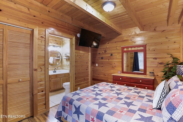 bedroom with connected bathroom, beamed ceiling, wood walls, light hardwood / wood-style floors, and wood ceiling