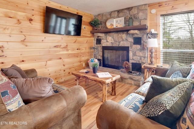 living room with a textured ceiling, hardwood / wood-style flooring, a stone fireplace, and wooden walls