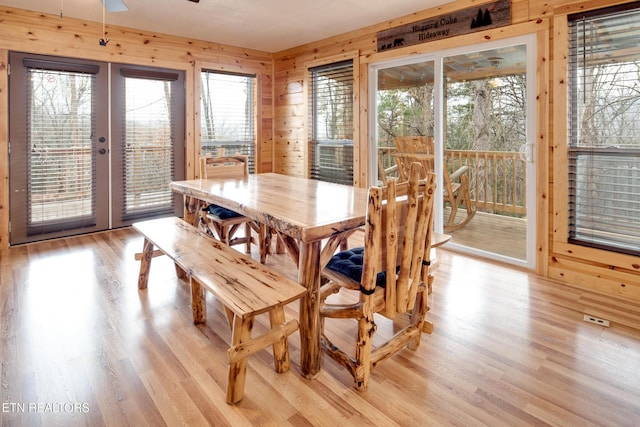 dining area with french doors, light hardwood / wood-style floors, ceiling fan, and wood walls