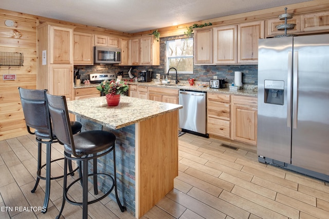 kitchen featuring light brown cabinets, sink, a kitchen island, light stone counters, and stainless steel appliances