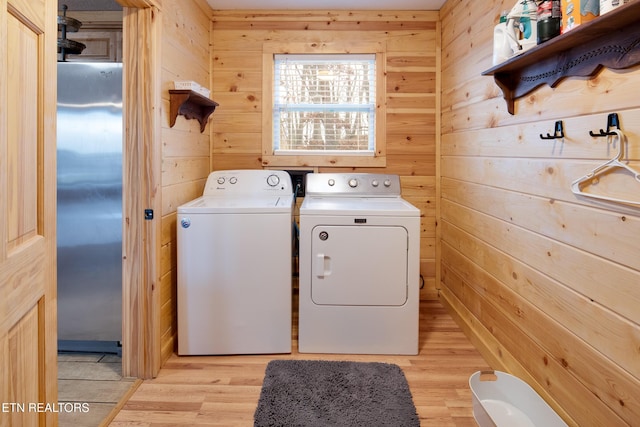 washroom with washer and dryer, light wood-type flooring, and wooden walls