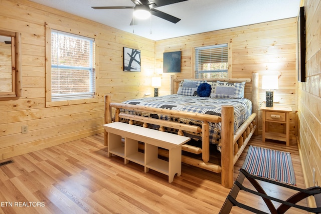 bedroom with ceiling fan, light wood-type flooring, and wooden walls