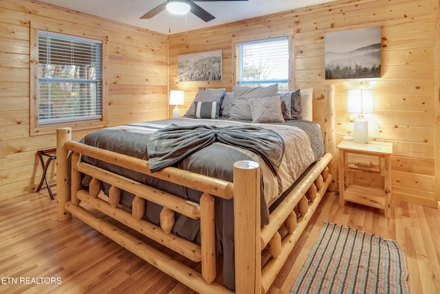 bedroom with ceiling fan, light hardwood / wood-style floors, and wood walls