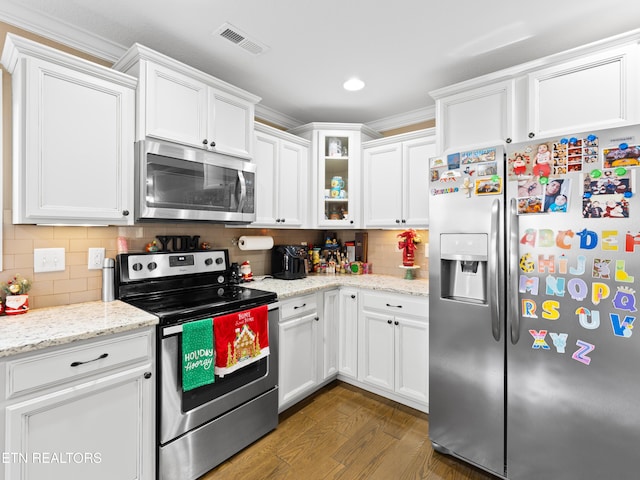 kitchen with appliances with stainless steel finishes, white cabinetry, ornamental molding, and dark wood-type flooring