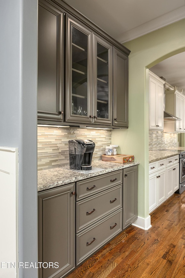 bar with white cabinets, dark hardwood / wood-style floors, ornamental molding, tasteful backsplash, and light stone counters