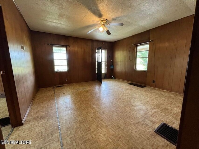 empty room with wood walls, ceiling fan, and a healthy amount of sunlight