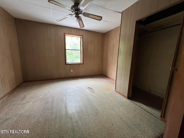 unfurnished bedroom featuring ceiling fan, light colored carpet, and wooden walls