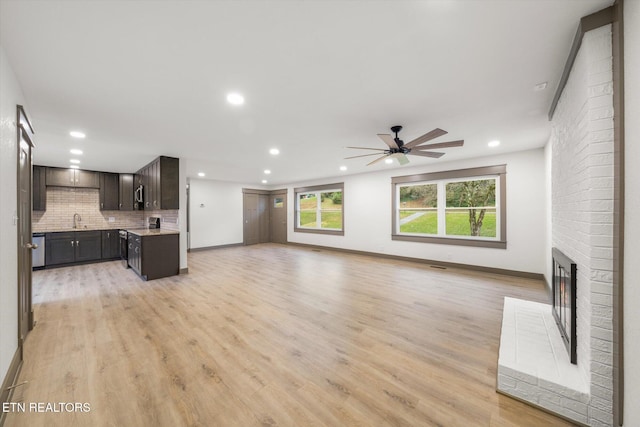 unfurnished living room with a fireplace, light wood-type flooring, ceiling fan, and sink