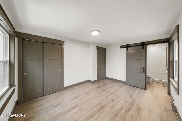 unfurnished bedroom with a barn door, light wood-type flooring, connected bathroom, and a closet