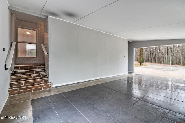 interior space featuring dark tile patterned floors, brick wall, and vaulted ceiling