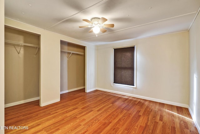 unfurnished bedroom with ceiling fan, light wood-type flooring, and two closets