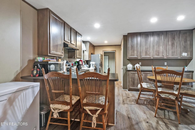 kitchen with dark brown cabinetry, light hardwood / wood-style floors, and appliances with stainless steel finishes