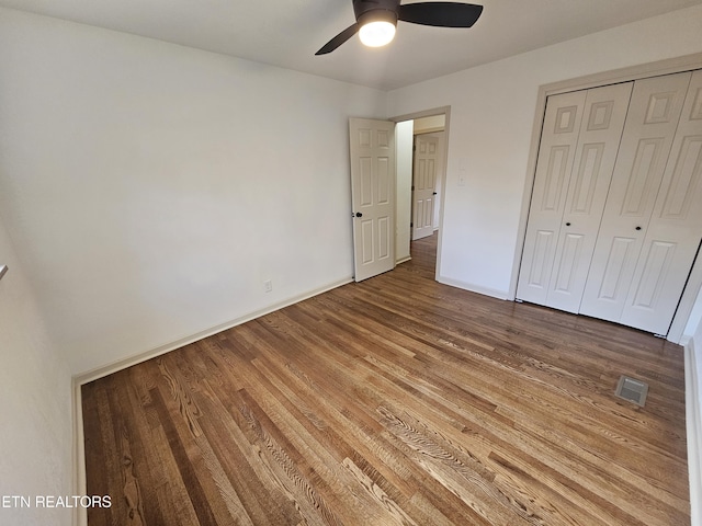 unfurnished bedroom with a closet, visible vents, ceiling fan, wood finished floors, and baseboards