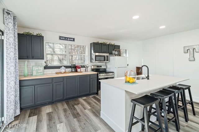 kitchen featuring an island with sink, stainless steel appliances, gray cabinets, and sink