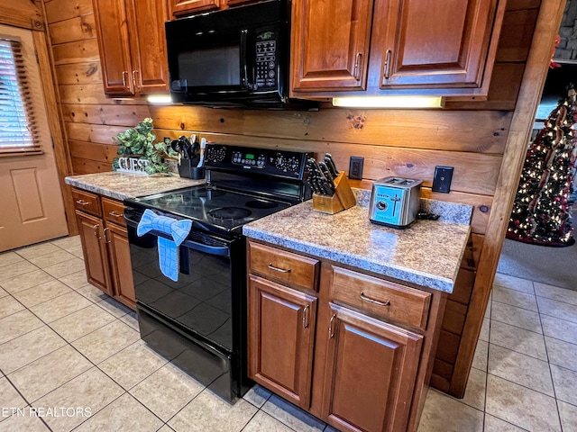 kitchen with light stone countertops, light tile patterned floors, wood walls, and black appliances