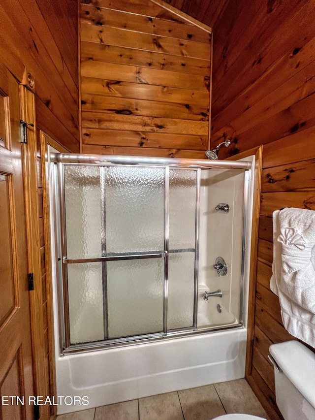 bathroom with tile patterned flooring, toilet, wooden walls, and enclosed tub / shower combo