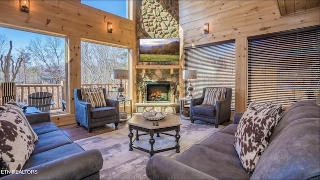 living room with hardwood / wood-style floors, high vaulted ceiling, an outdoor stone fireplace, and wooden walls