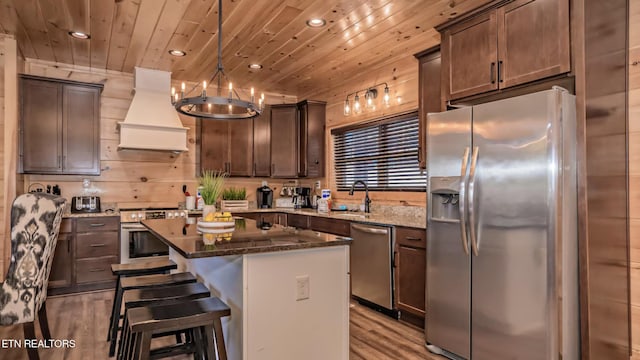 kitchen with custom exhaust hood, hanging light fixtures, dark stone countertops, appliances with stainless steel finishes, and a kitchen island