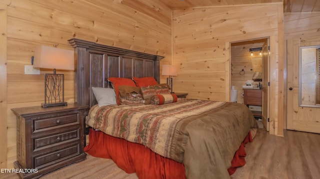 bedroom with hardwood / wood-style flooring, ensuite bathroom, wood walls, and lofted ceiling