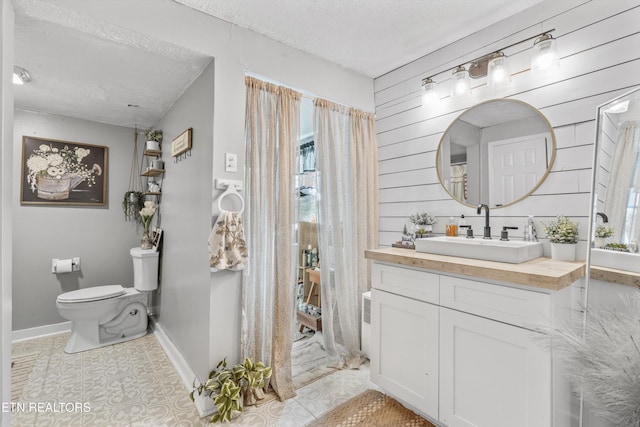 bathroom with vanity, wood walls, toilet, and a textured ceiling