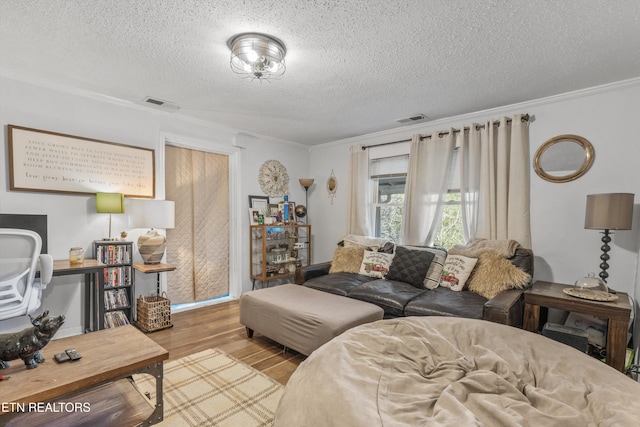 living room featuring light wood-type flooring, a textured ceiling, and ornamental molding