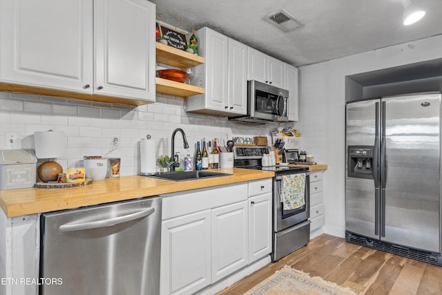 kitchen featuring backsplash, wooden counters, white cabinets, light wood-type flooring, and stainless steel appliances