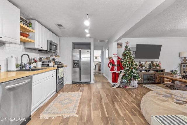 kitchen with backsplash, a textured ceiling, stainless steel appliances, light hardwood / wood-style floors, and white cabinetry