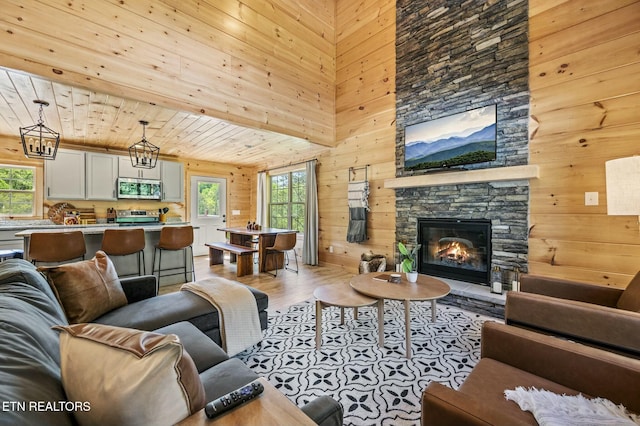 living room with a notable chandelier, wooden ceiling, light hardwood / wood-style floors, a stone fireplace, and wood walls