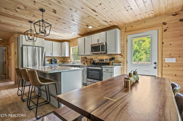 kitchen featuring wood walls, hanging light fixtures, hardwood / wood-style flooring, appliances with stainless steel finishes, and a kitchen island