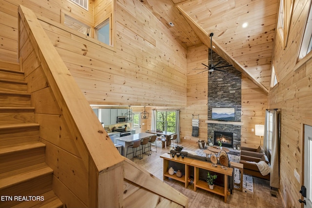 living room with wood ceiling, wooden walls, wood-type flooring, high vaulted ceiling, and a fireplace