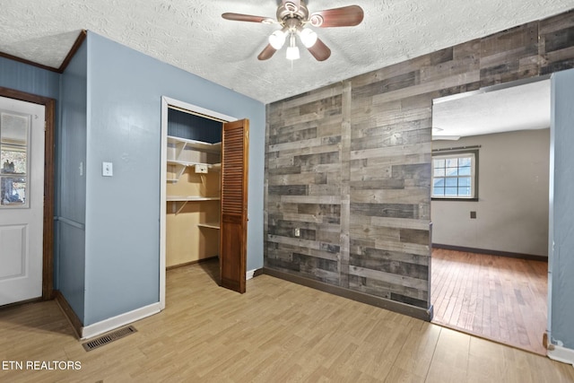 interior space featuring wood walls, ceiling fan, light hardwood / wood-style floors, and a textured ceiling