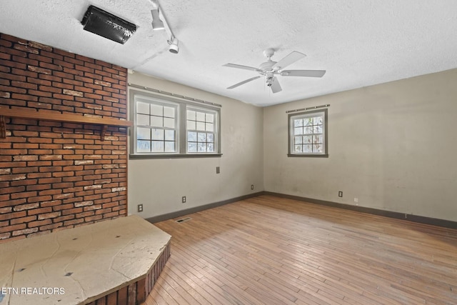 unfurnished living room featuring a textured ceiling, light wood-type flooring, ceiling fan, and brick wall