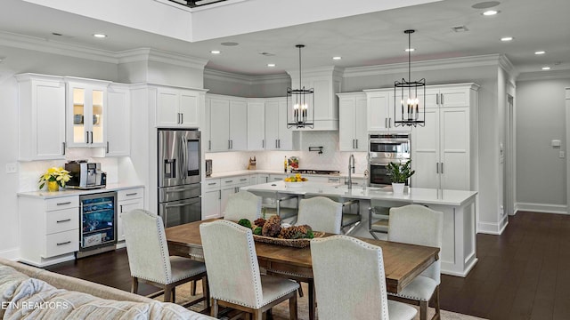 kitchen with a center island with sink, white cabinets, hanging light fixtures, dark hardwood / wood-style flooring, and beverage cooler