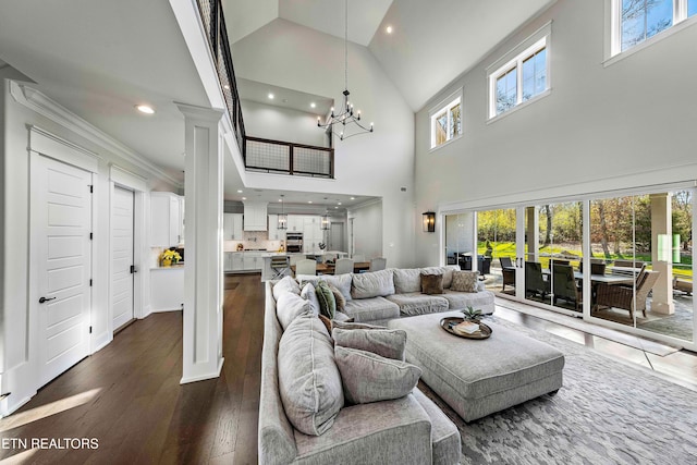 living room featuring decorative columns, ornamental molding, an inviting chandelier, high vaulted ceiling, and hardwood / wood-style floors