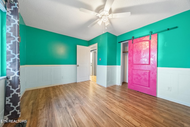 spare room featuring ceiling fan, a barn door, light hardwood / wood-style floors, and a textured ceiling