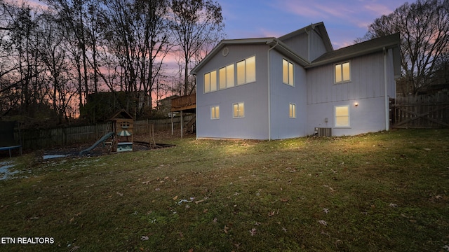 back house at dusk with a playground, a trampoline, central AC, and a lawn