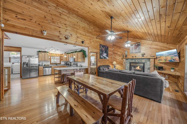 dining space featuring high vaulted ceiling, wooden walls, light wood-type flooring, a fireplace, and washer / dryer