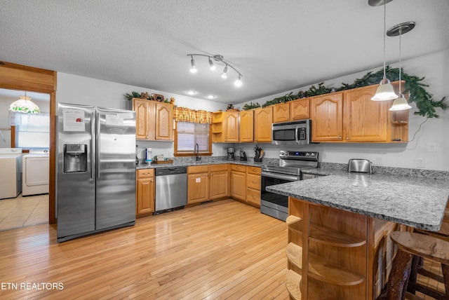 kitchen featuring washer and dryer, stainless steel appliances, hanging light fixtures, and light hardwood / wood-style floors