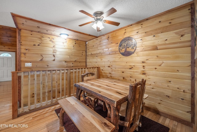 dining space featuring wooden walls, ceiling fan, light hardwood / wood-style floors, and a textured ceiling