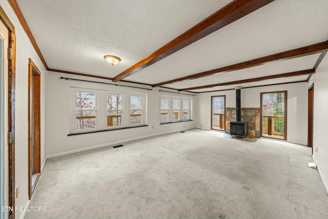 unfurnished living room featuring a wood stove, crown molding, carpet flooring, a textured ceiling, and beamed ceiling