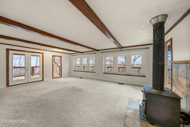 unfurnished living room with light carpet, ornamental molding, a textured ceiling, beam ceiling, and a wood stove