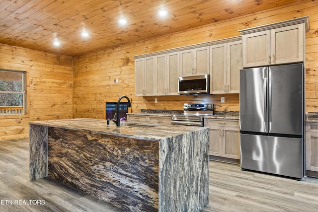 kitchen with sink, stainless steel appliances, dark stone counters, light hardwood / wood-style floors, and wooden walls