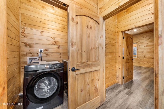 clothes washing area with washing machine and dryer, wood walls, and wood-type flooring