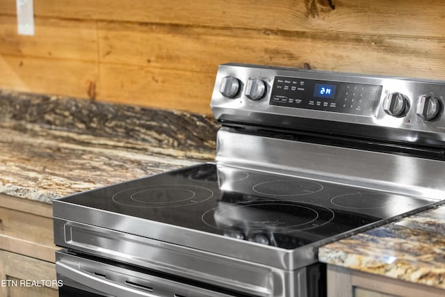 details with light brown cabinetry, electric range, wooden walls, and stone counters