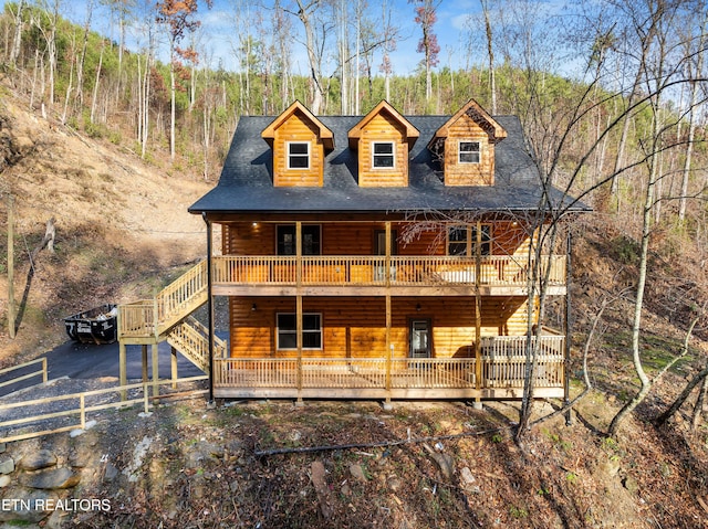 view of front of house with a shingled roof, a wooden deck, and faux log siding