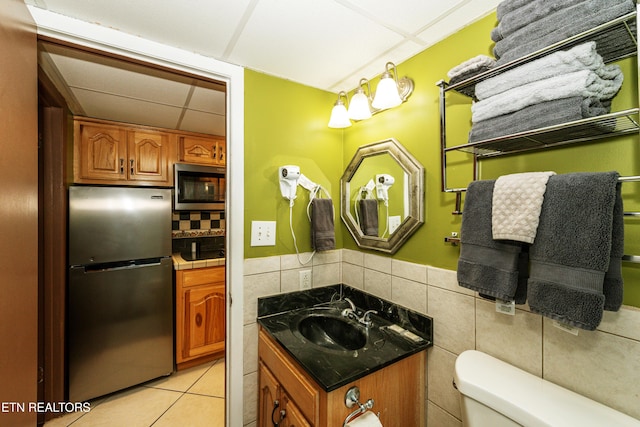 bathroom featuring a drop ceiling, vanity, backsplash, tile patterned floors, and toilet