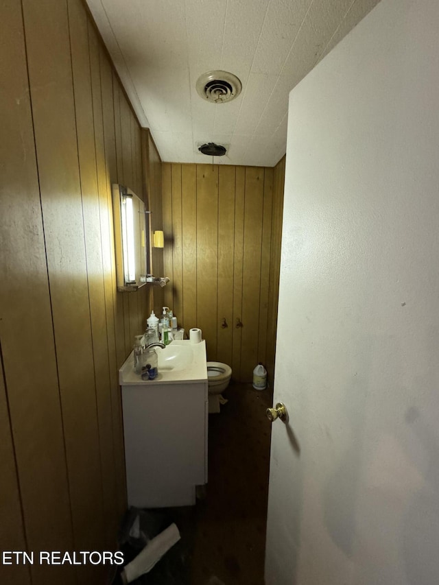 bathroom with vanity, toilet, and wood walls