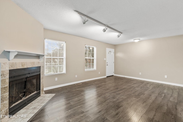 unfurnished living room featuring dark hardwood / wood-style flooring, rail lighting, a textured ceiling, and a tiled fireplace