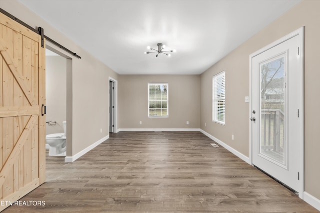 unfurnished dining area with hardwood / wood-style floors, a barn door, and an inviting chandelier