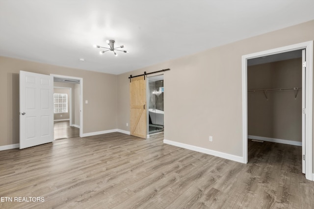 unfurnished bedroom featuring ensuite bathroom, a barn door, a spacious closet, light hardwood / wood-style flooring, and a closet